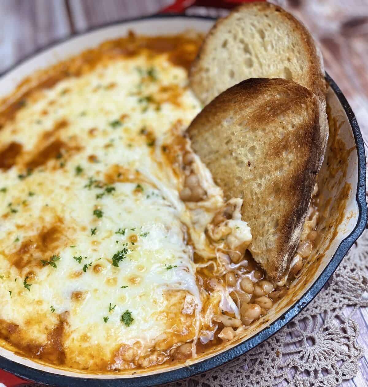 Two pieces of toast inserted into the cheese and beans in a skillet.