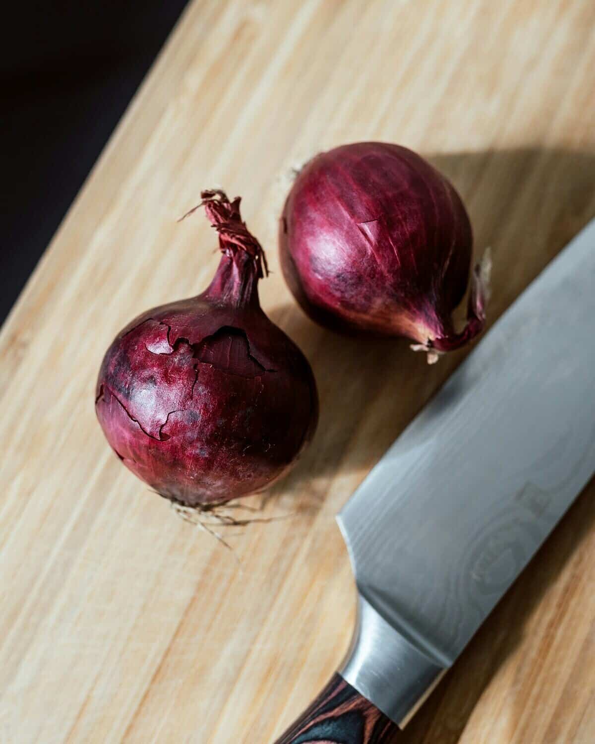 Two onions and a sharp knife on a cutting board.