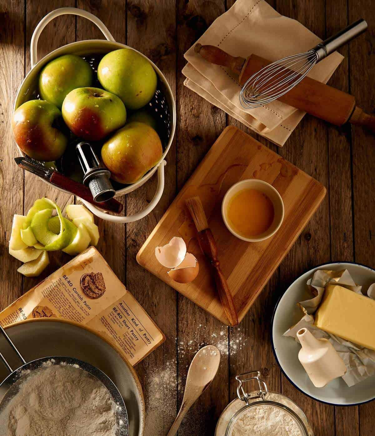 Kitchen tools and bowls with food placed about on a tabletop.