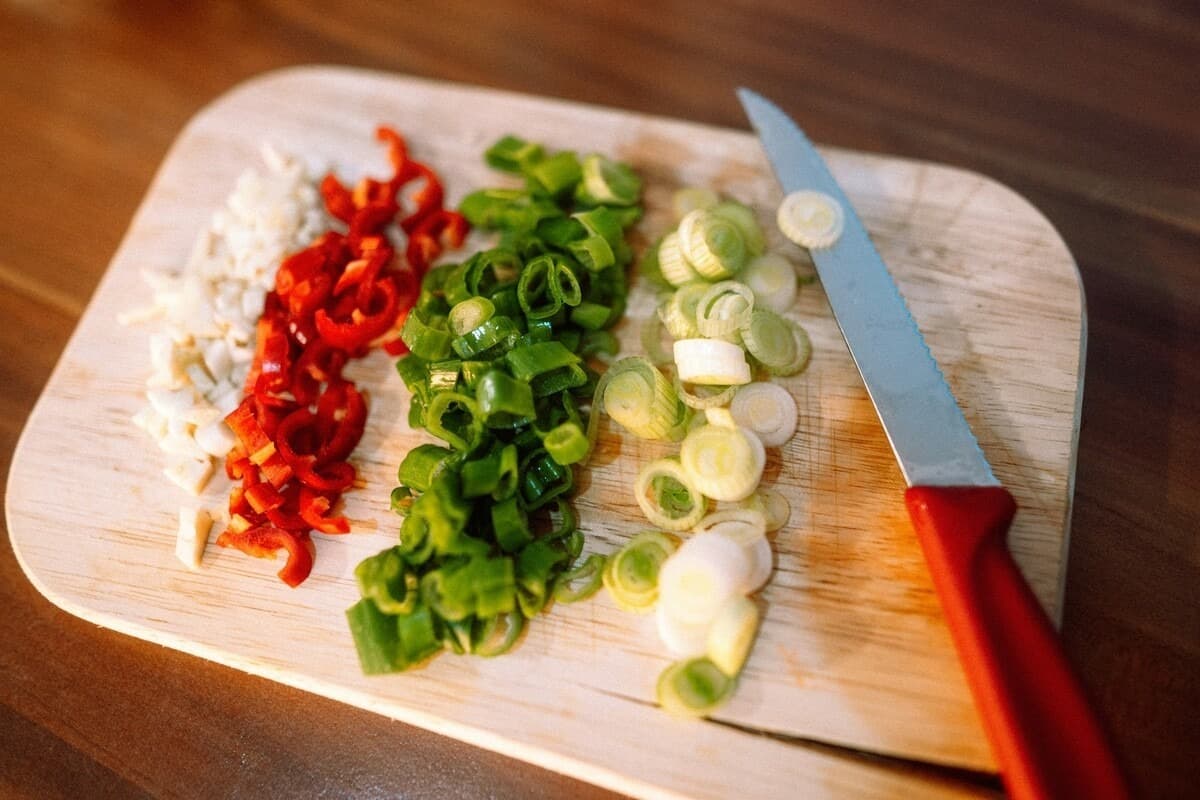 Four vegetables sliced up and laid in rows alongside a knife on a cutting board.