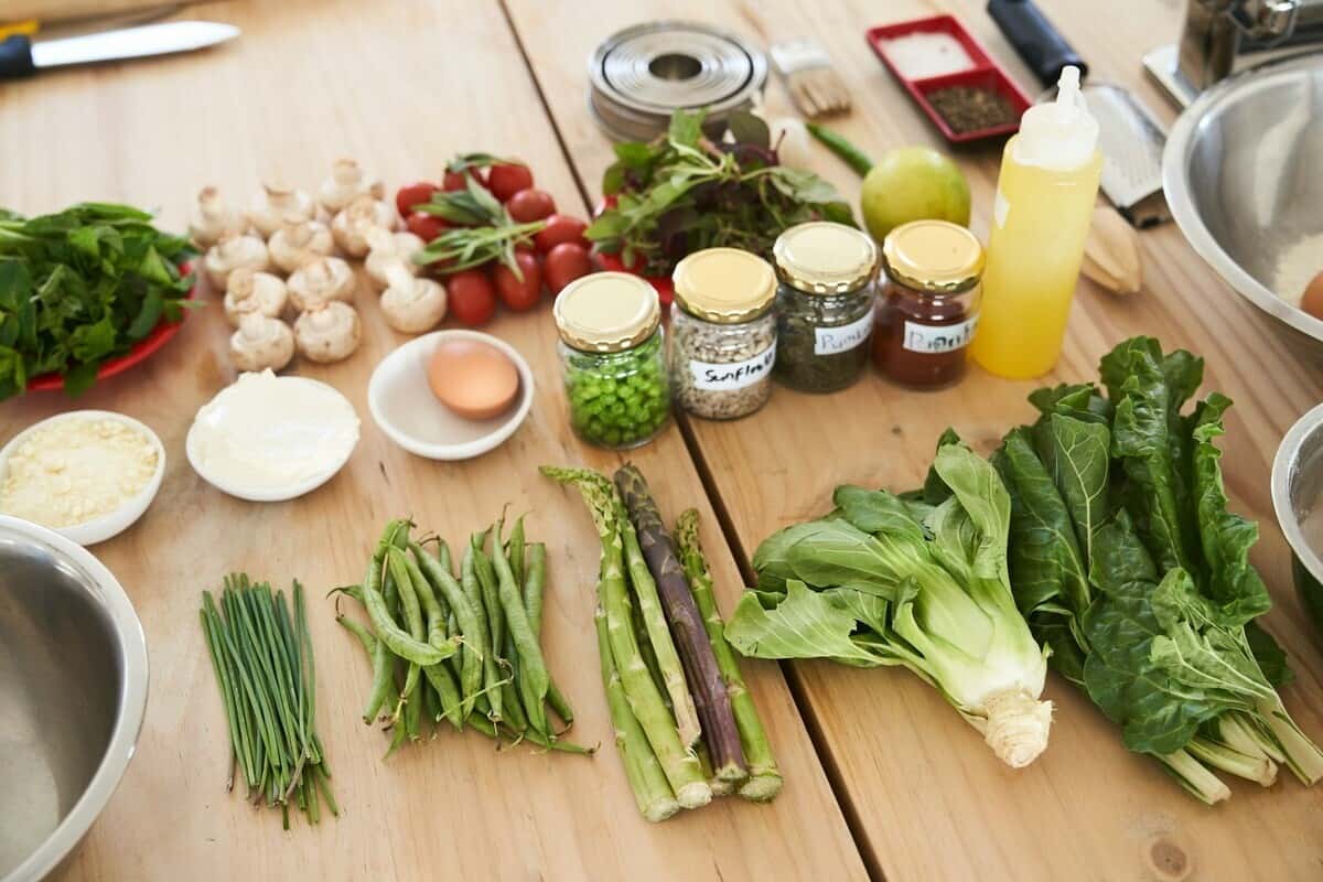 Vegetables, seasoning jars and bowls lined up on a counter for mise en place preparation.