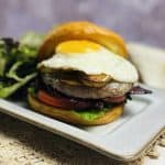 A loaded cheeseburger on a plate with a salad.