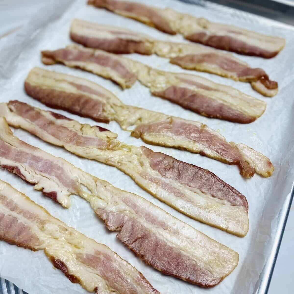 Bacon slices lined up on a sheetpan over parchment.