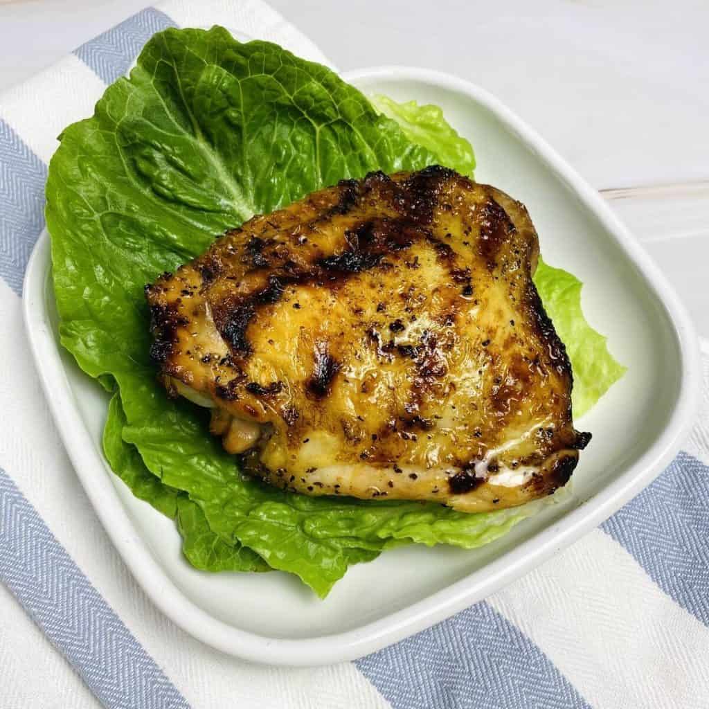 A mesquite grilled chicken thigh on a piece of lettuce on a plate.