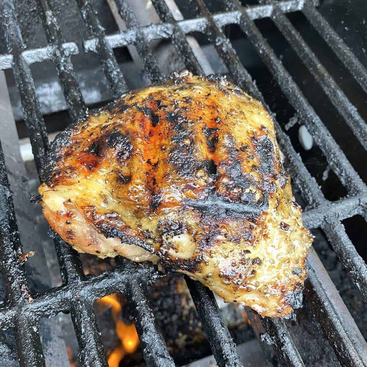 A chicken thigh cooking on the bbq grill.