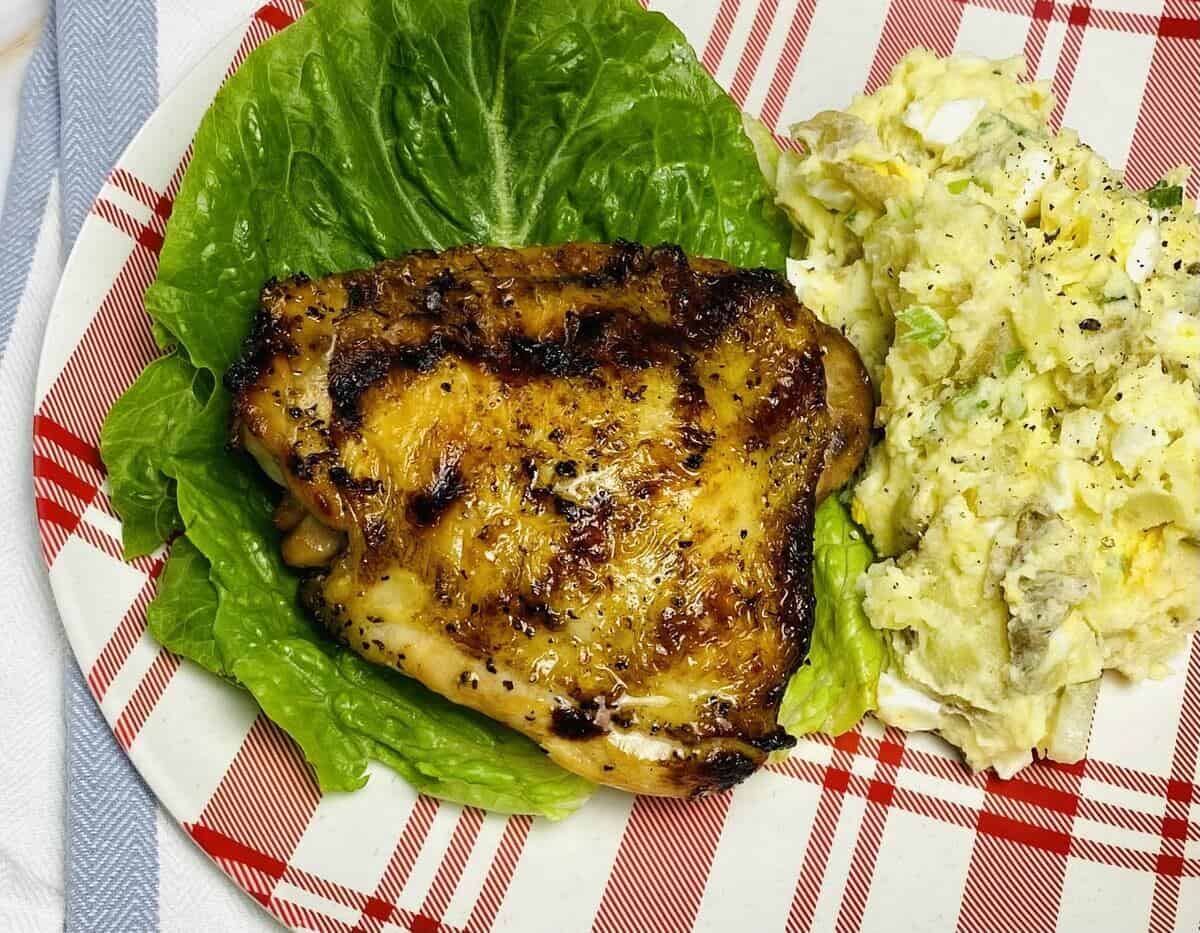 A grilled chicken thigh on a plate with salad.