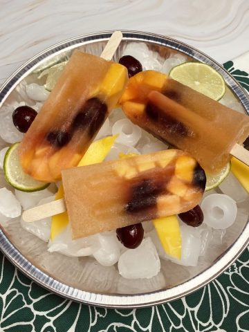 Three white sangria popsicles sitting on a tray of ice garnished with fresh fruit.