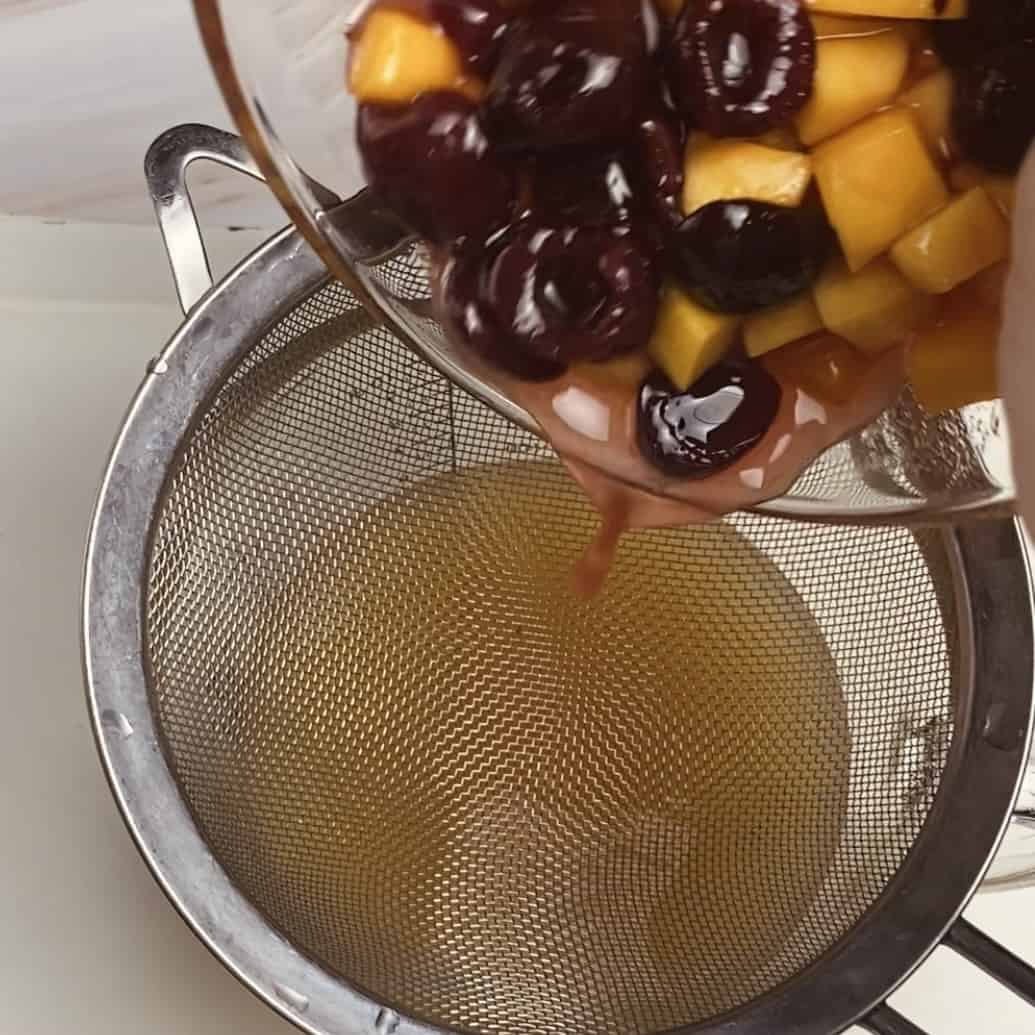 A bowl of sugared fruit being poured into a strainer on a juice pitcher.