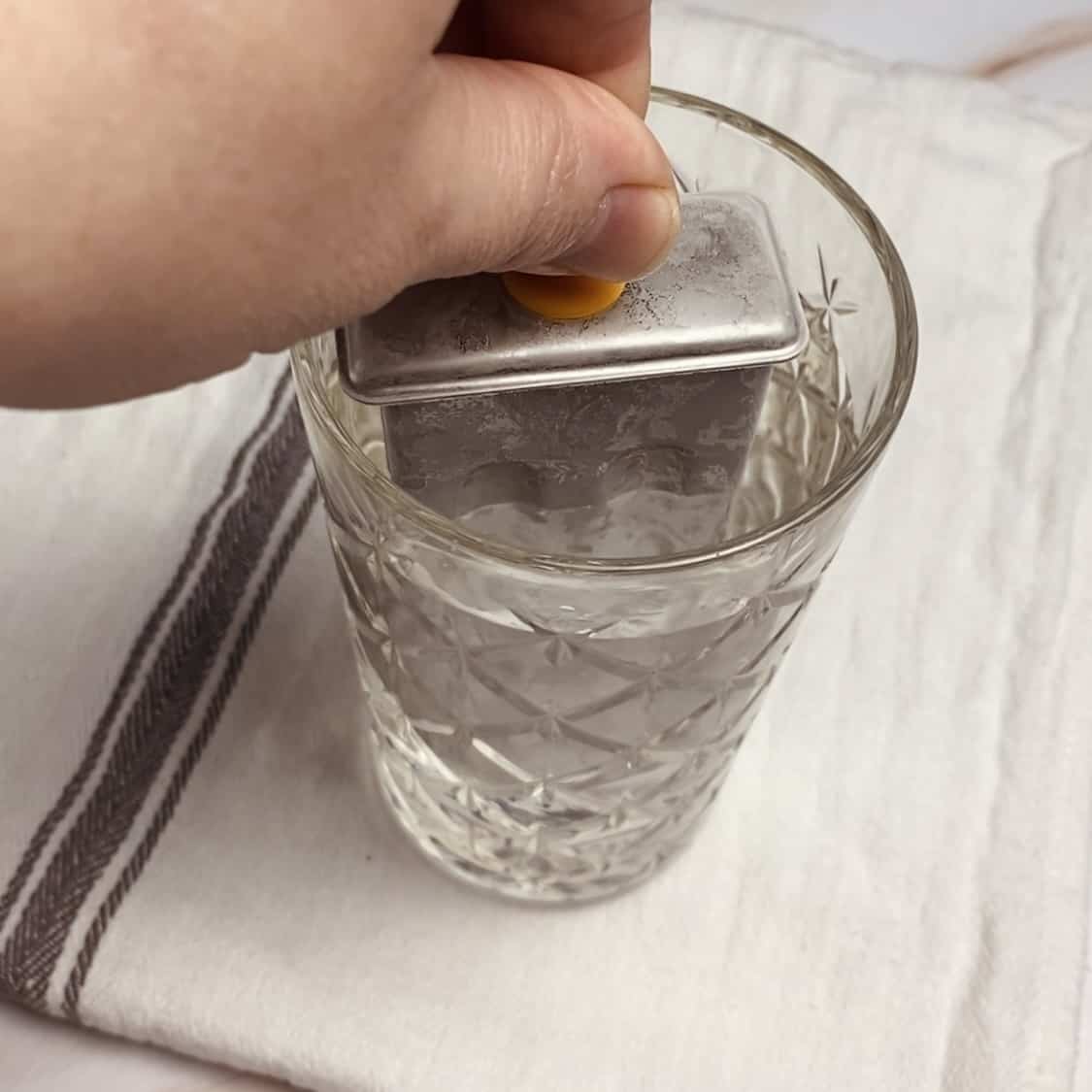 A frozen metal popsicle mold getting dipped in a glass of water.