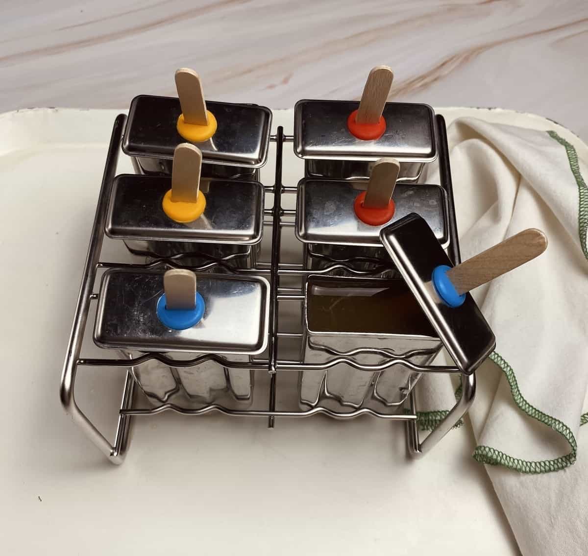 A metal popsicle tray filled with punch with sticks inserted.