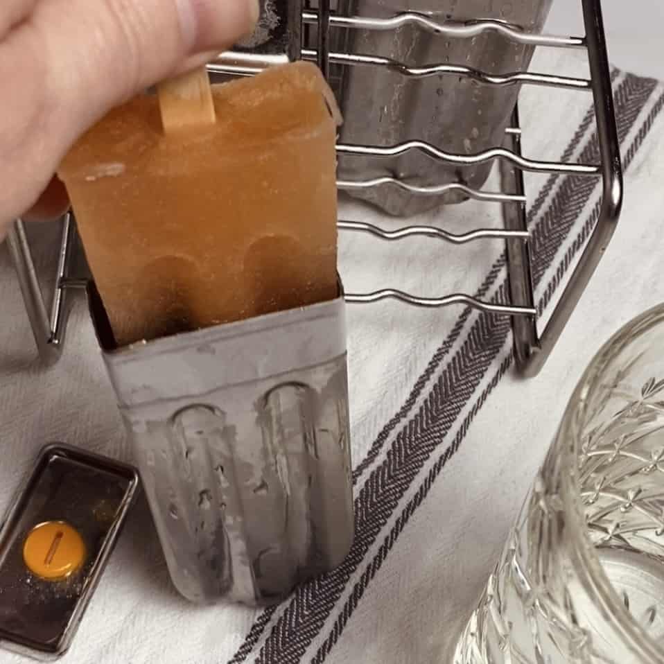 A hand pulling the popsicle out of a metal mold over a towel.