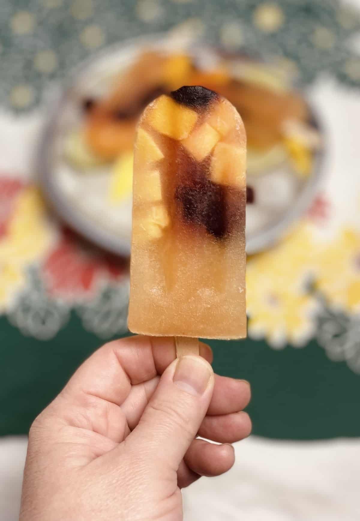 A hand holding up a single popsicle with a tray of. more popsicles in the background.