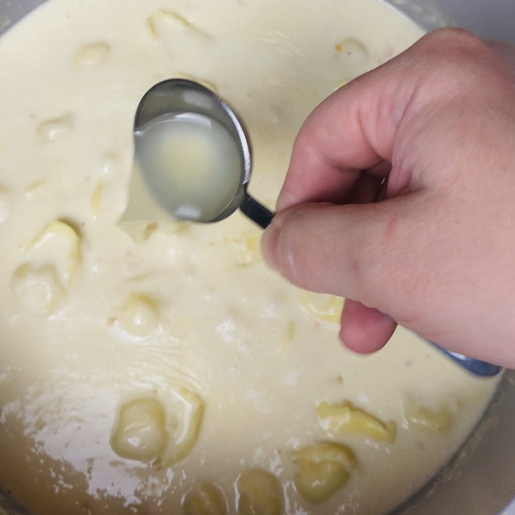 A pot of creamy tortellini soup with lemon juice being poured in.