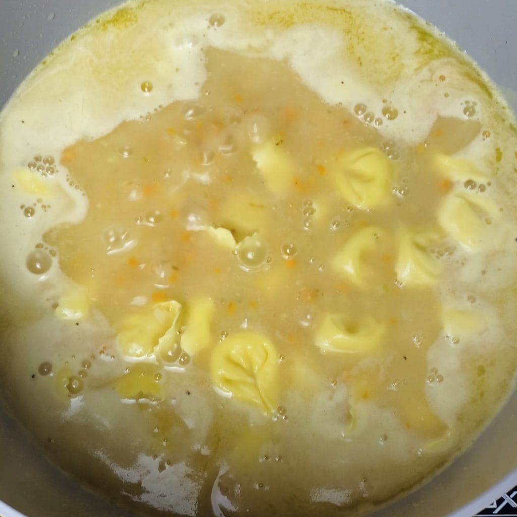 A pot of brothy soup with tortellini.