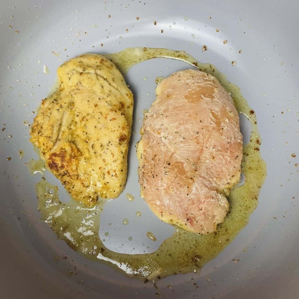 Two pieces of chicken cooking in butter in a pot.