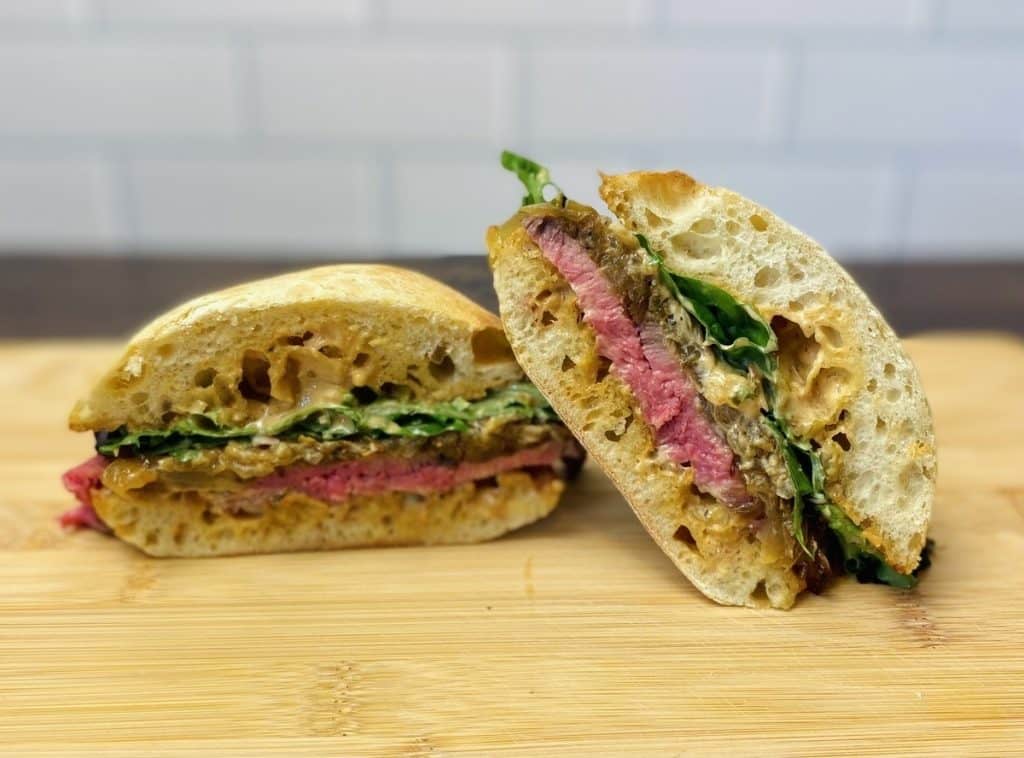 A steak sandwich sliced in half on a cutting board.