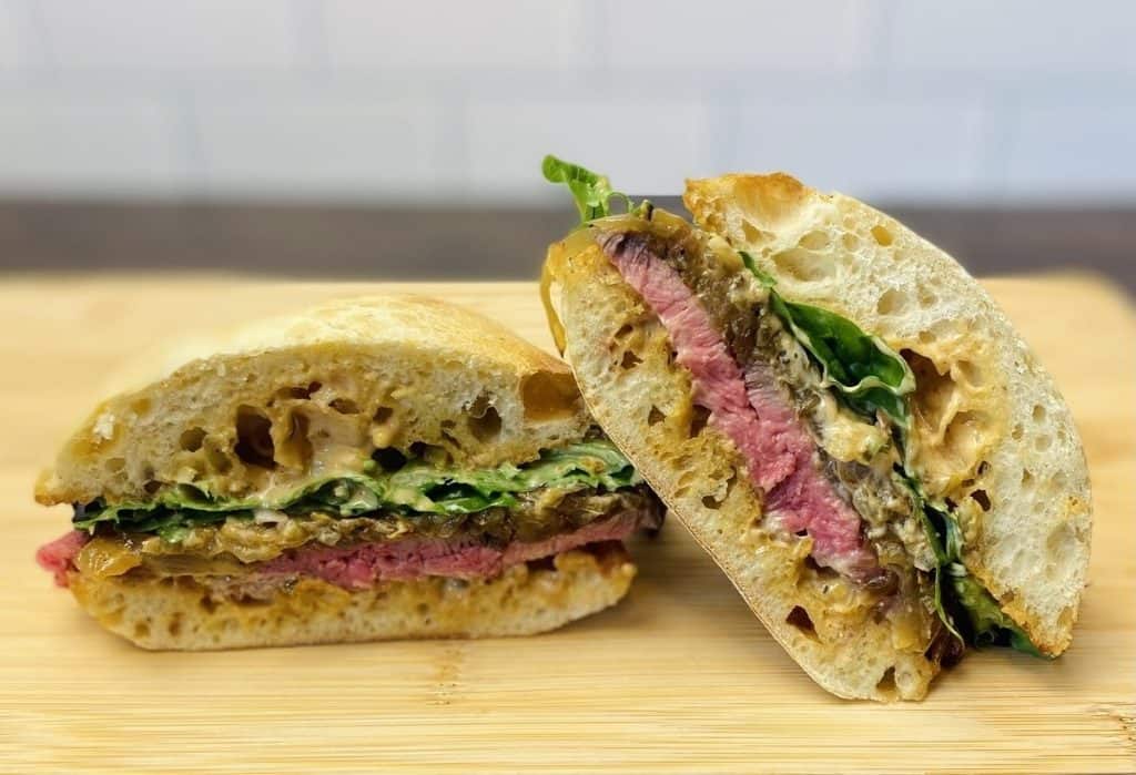 Two halves of a steak sandwich on a cutting board.