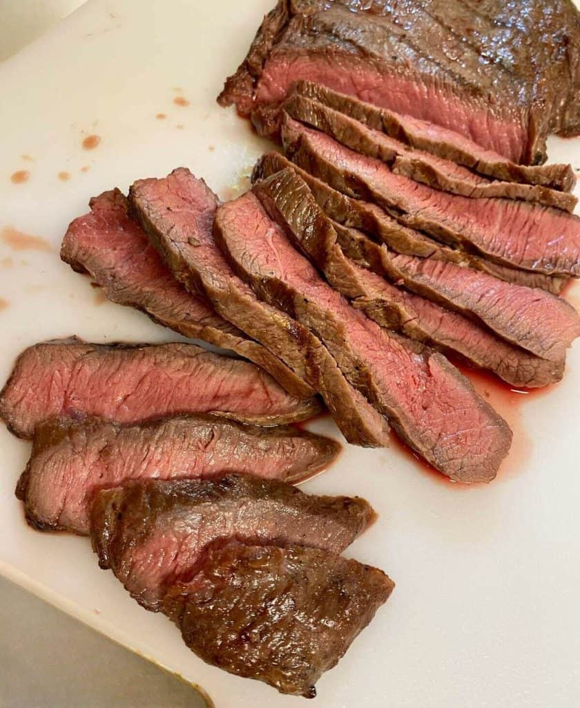 A flat iron steak sliced into thin pieces on a cutting board.