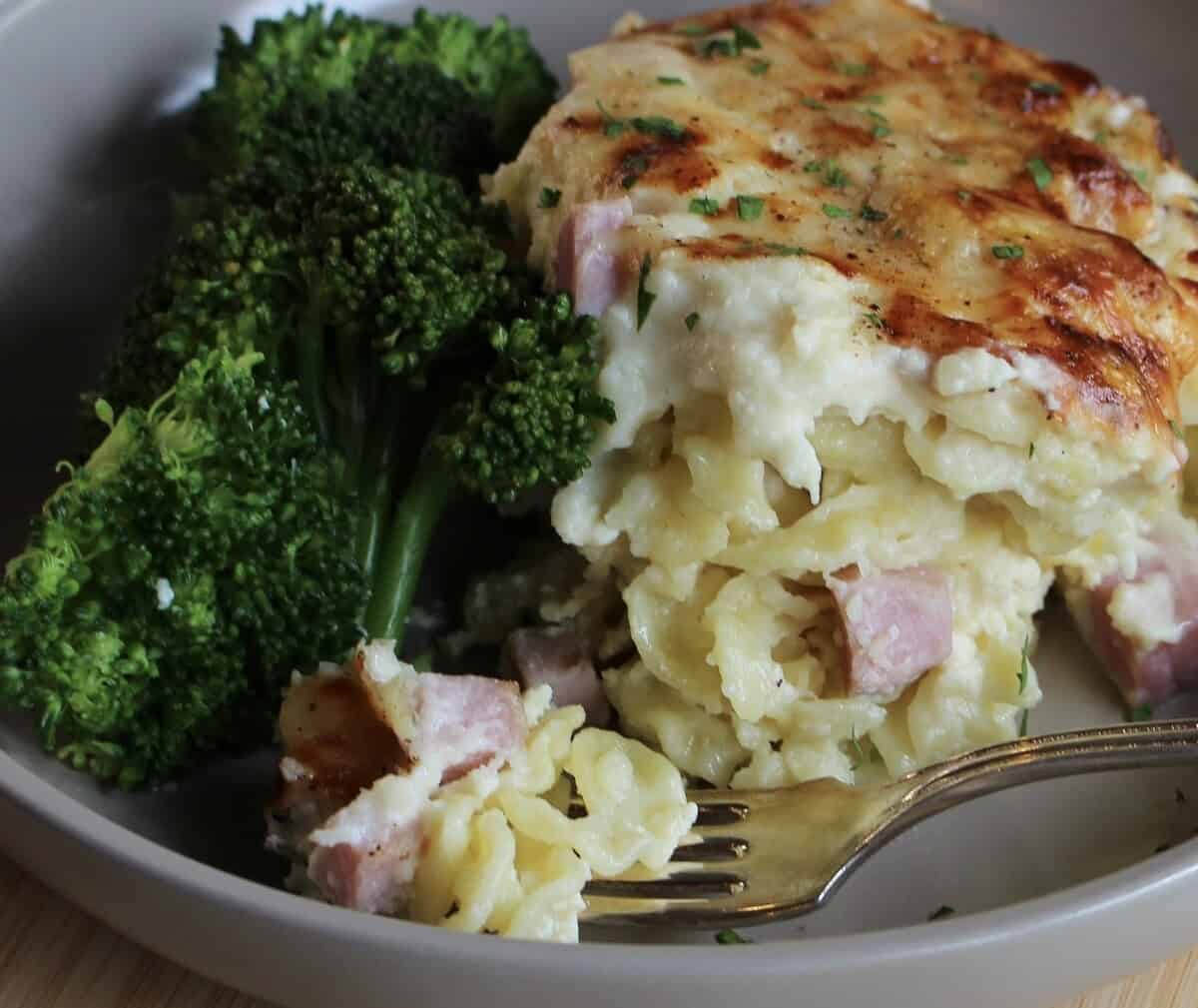 A scoop of pasta bake on a plate with broccoli and a fork.