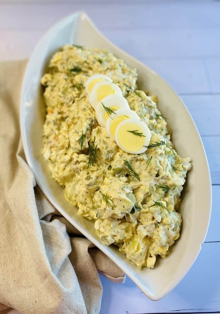 A dish of potato salad with sliced eggs and fresh herbs on top alongside a napkin.