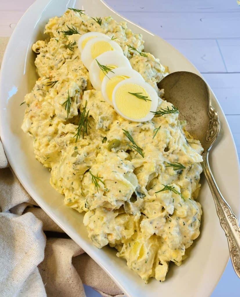 A long bowl of triple tater salad with a silver serving spoon rested inside.