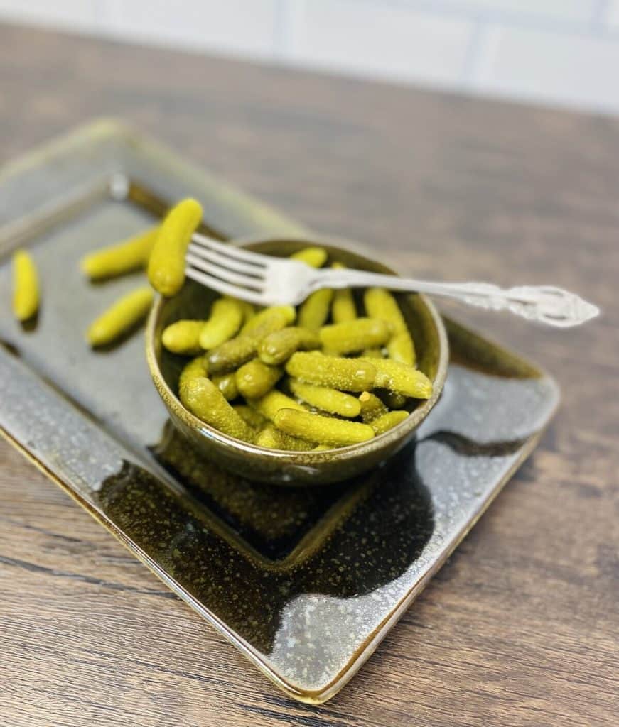 A bowl of cornichon pickles and a fork.