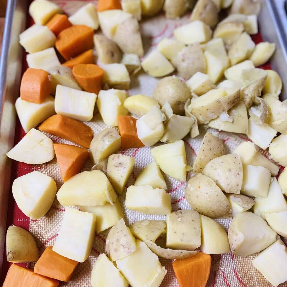 A sheet pan with yams and potatoes cooling.