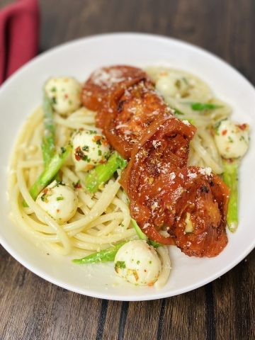 A plate with asparagus and tomato pasta alongside a spoon and napkin.