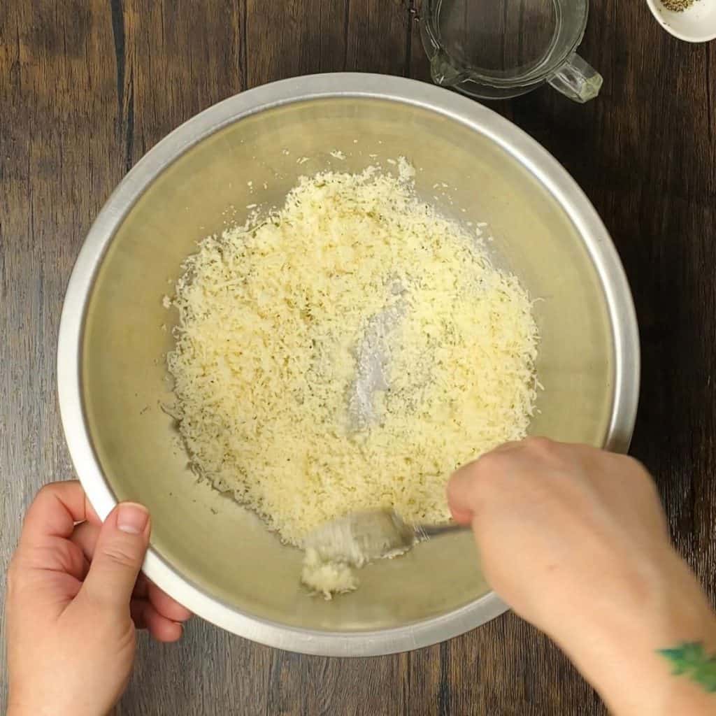 A hand stirring water into a bowl of grated parmesan.