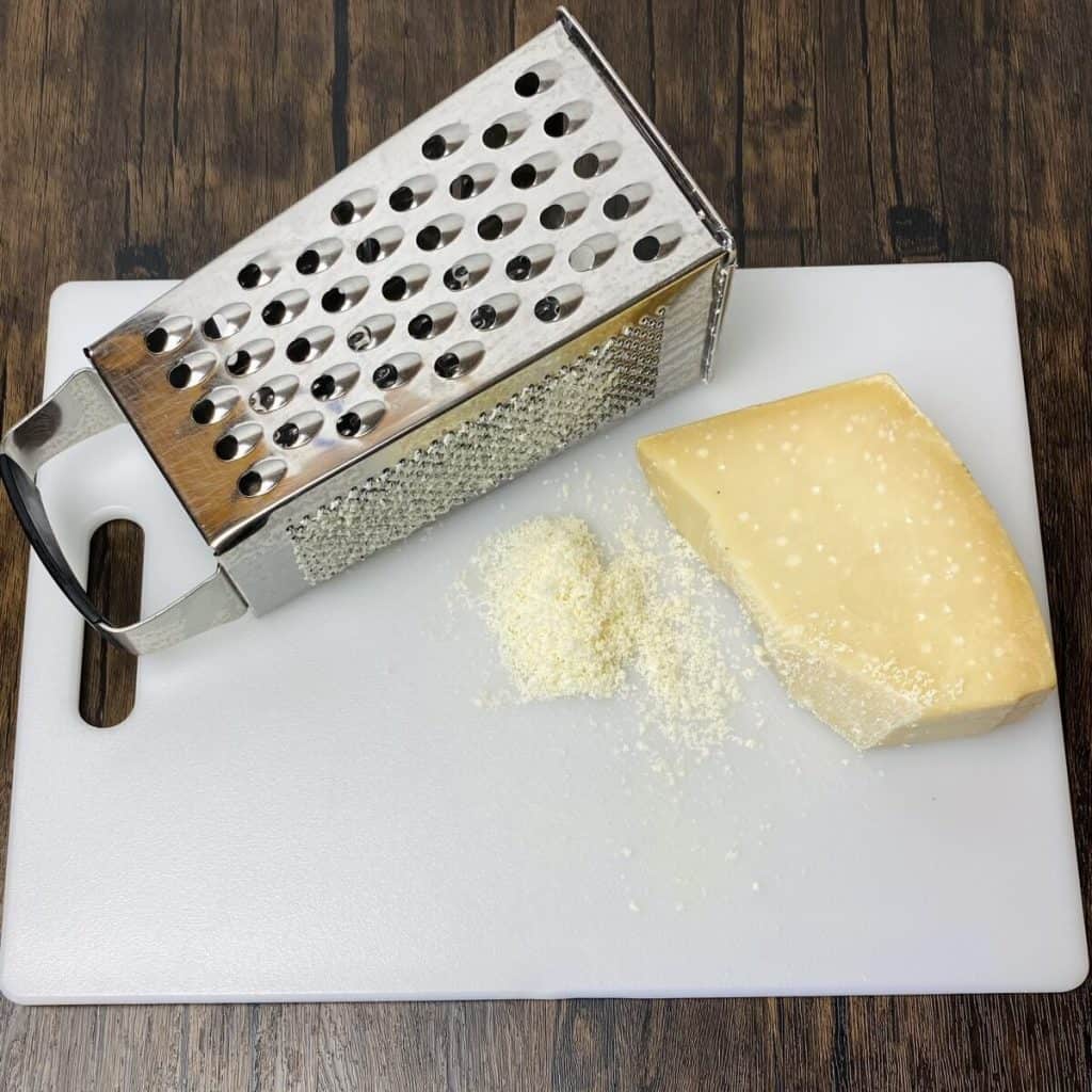 A cutting board with a wedge of parmesan alongside a cheese grater.