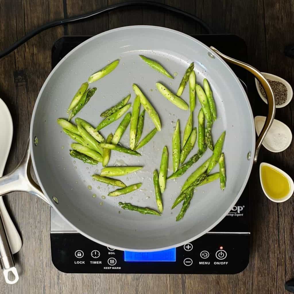 Asparagus pieces frying in a skillet on a burner.