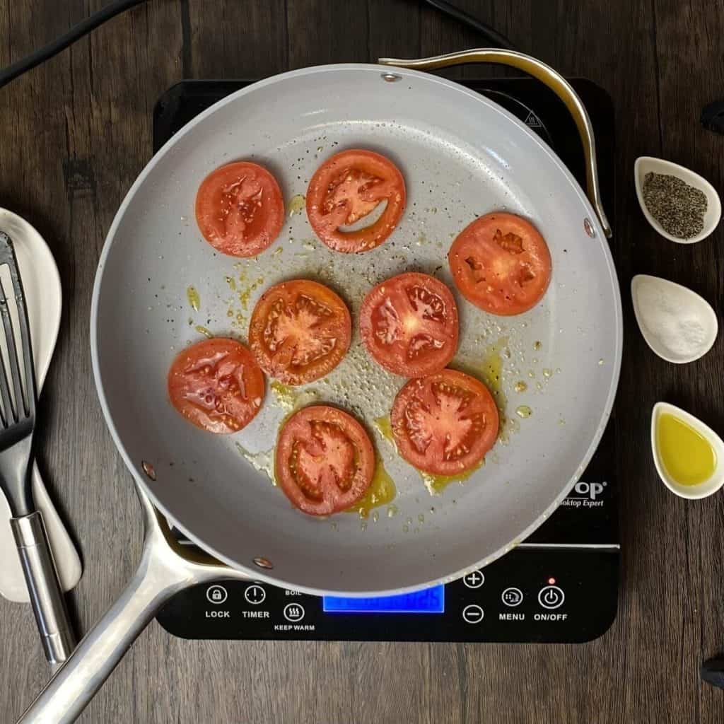 Tomato slices searing in a skillet on a burner.