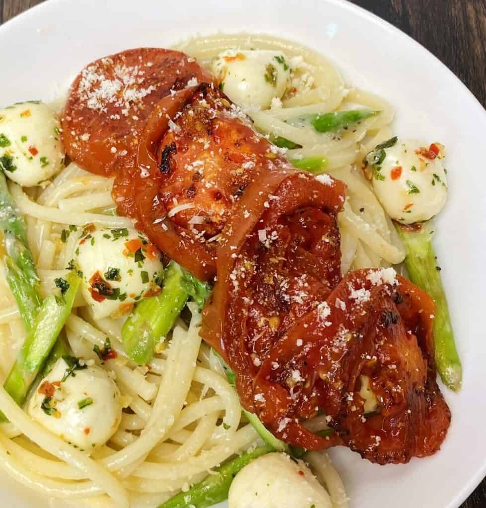 A closeup of seared sliced tomatoes on top of a plate of pasta.