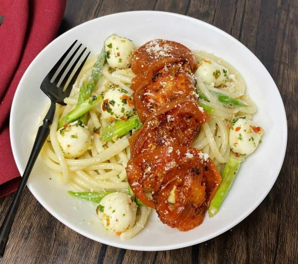 A bowl of pasta with mozzarella balls and sliced tomatoes on top.