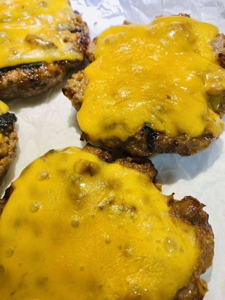 Burger patties on a plate with melted cheddar on top.