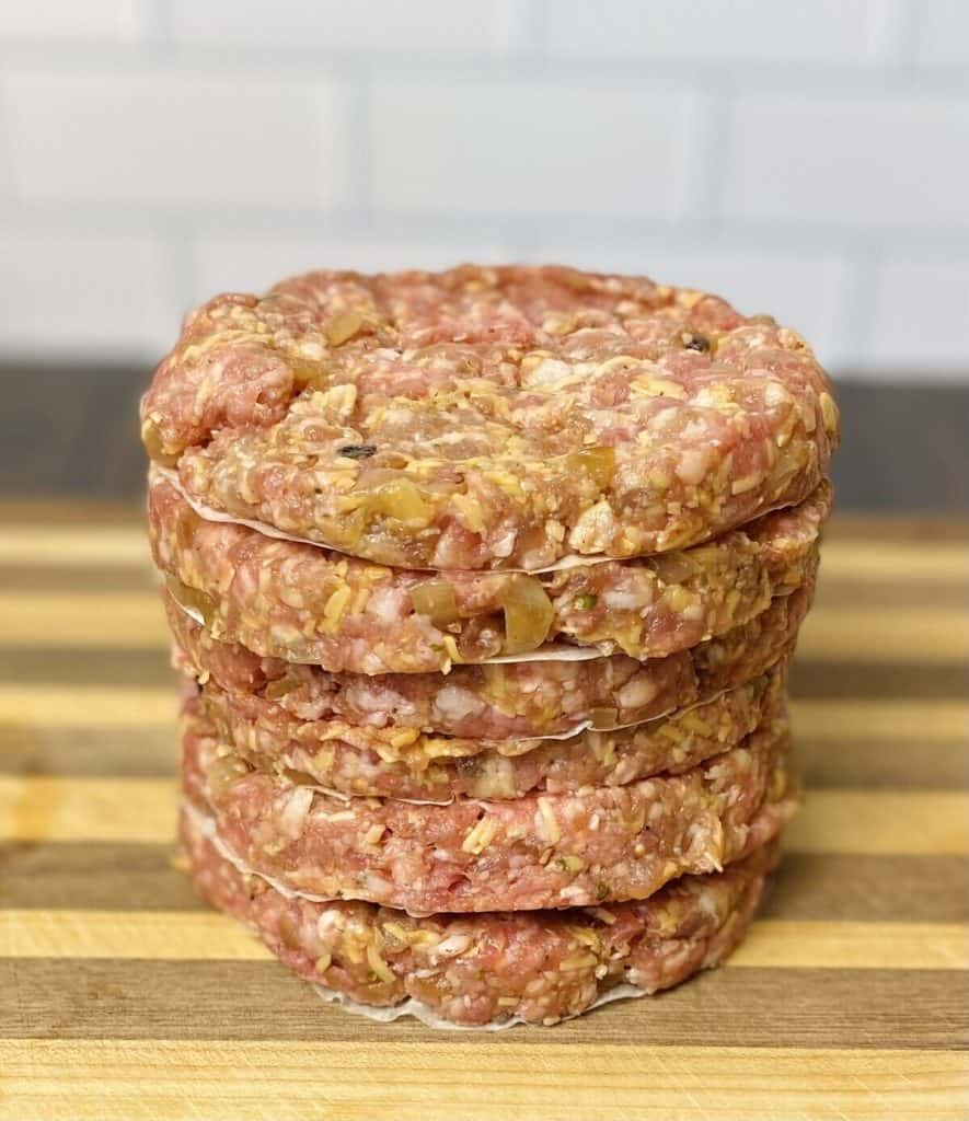 A stack of raw burger bbq cheddar burger patties on a cutting board.