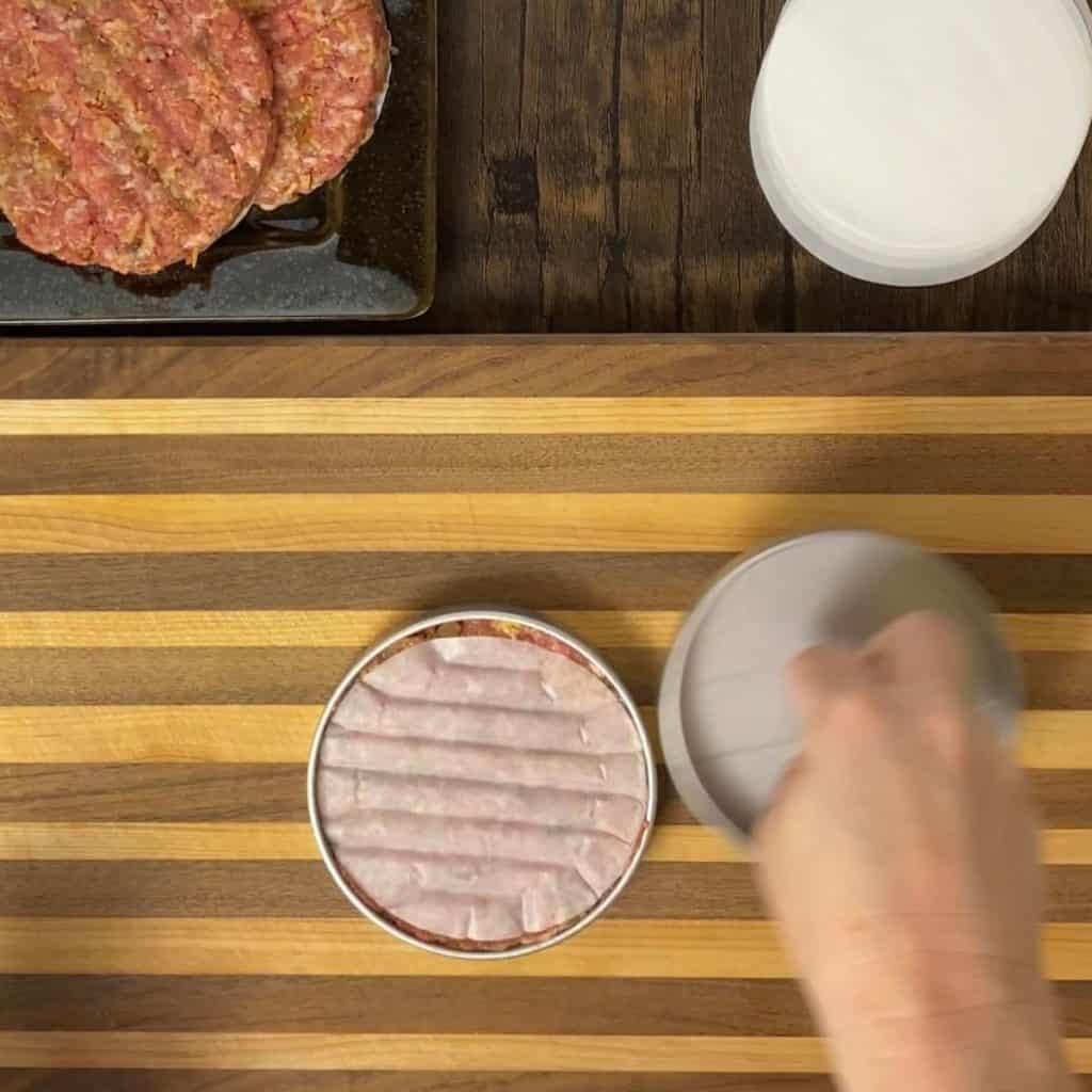 Raw burger in a burger press on a cutting board.