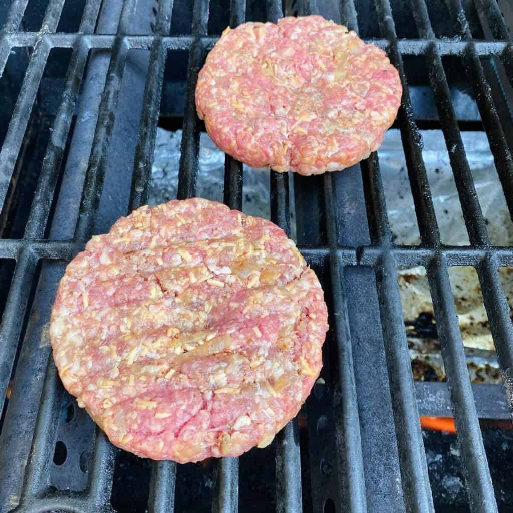 Two raw burger patties on a bbq grill.