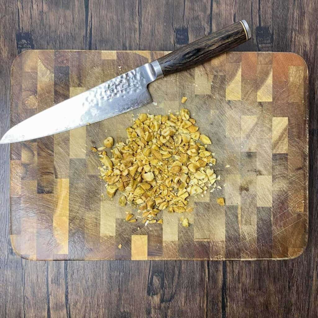 Nuts chopped up on a cutting board with a knife.