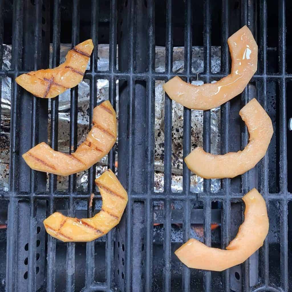 Six slices of cantaloupe on a bbq grill.