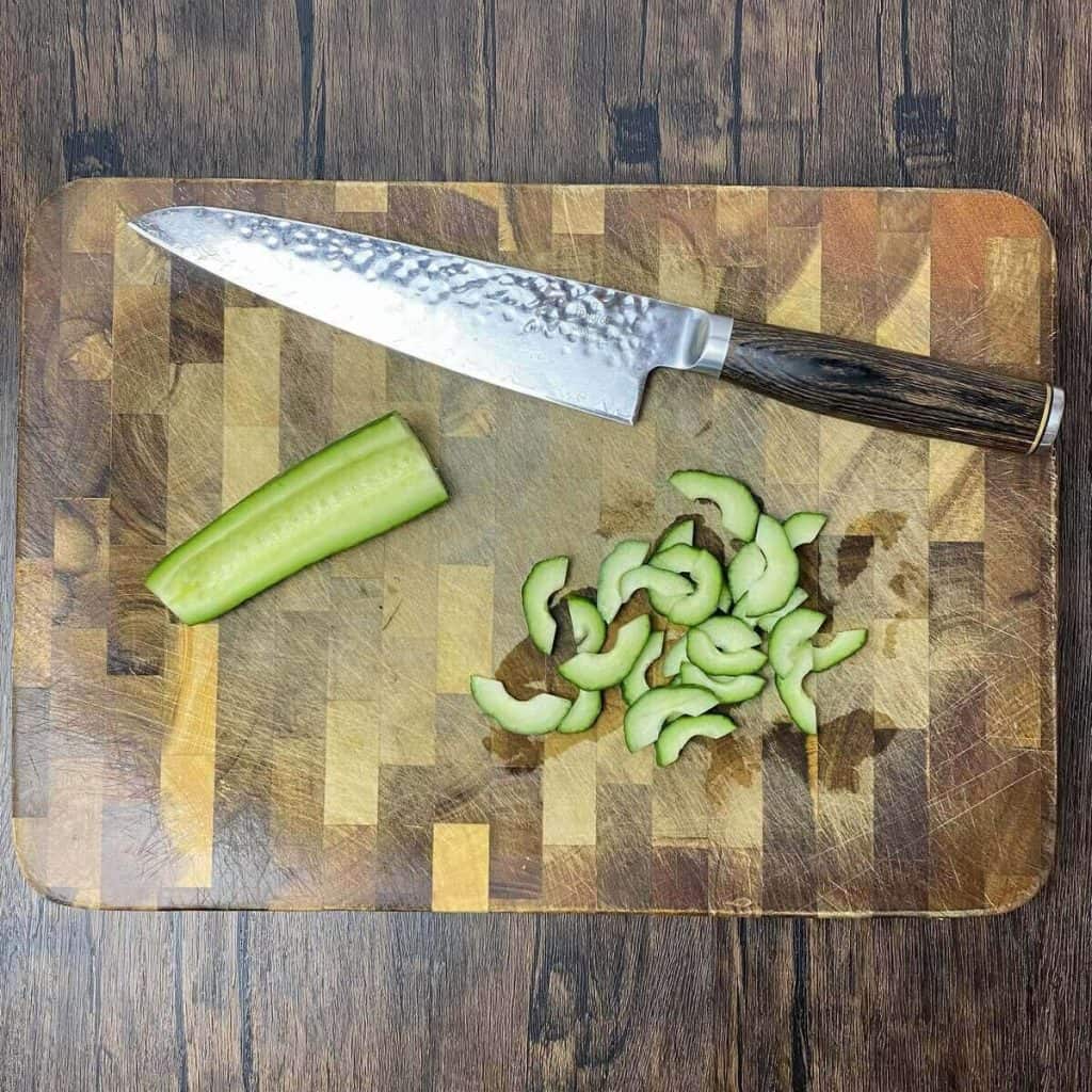 Cucumber sliced on a cutting board with a knife.