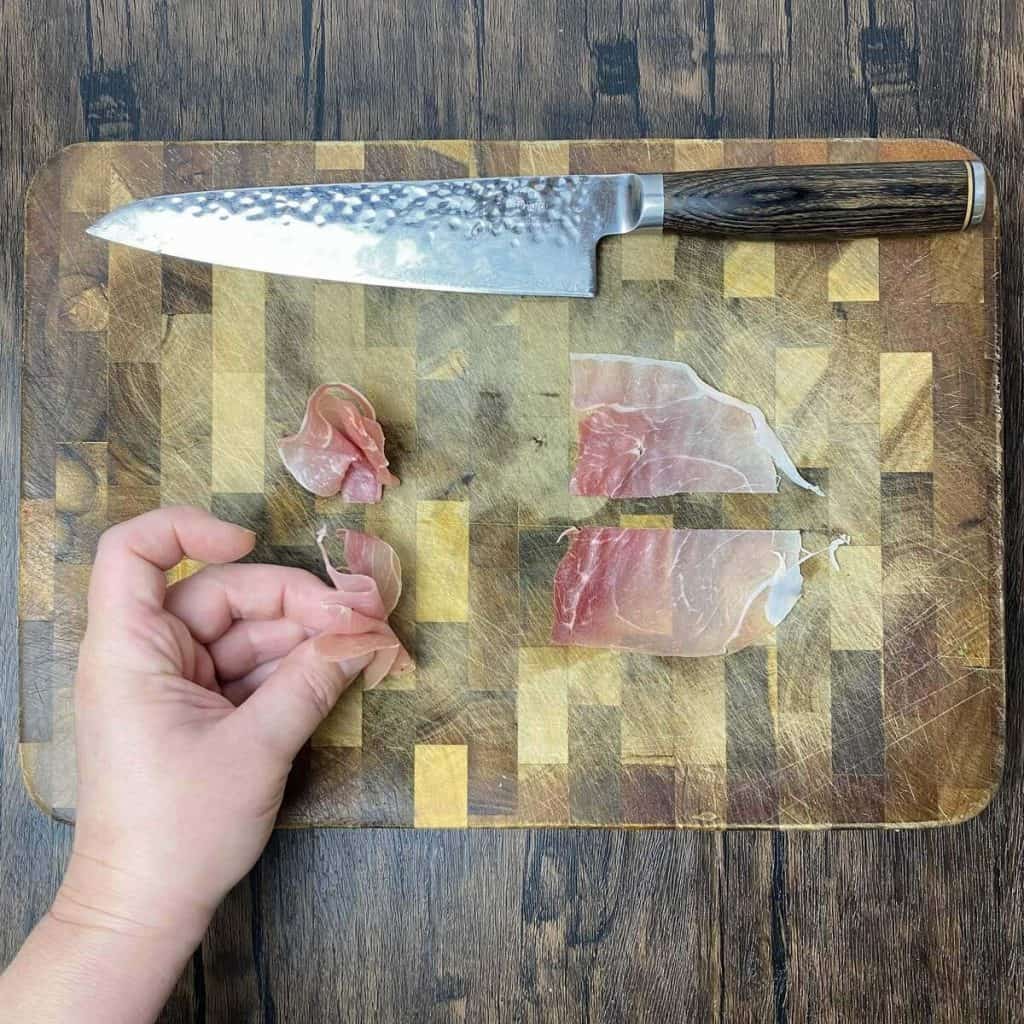 Prosciutto sliced on a cutting board with a hand showing how to fold it up.