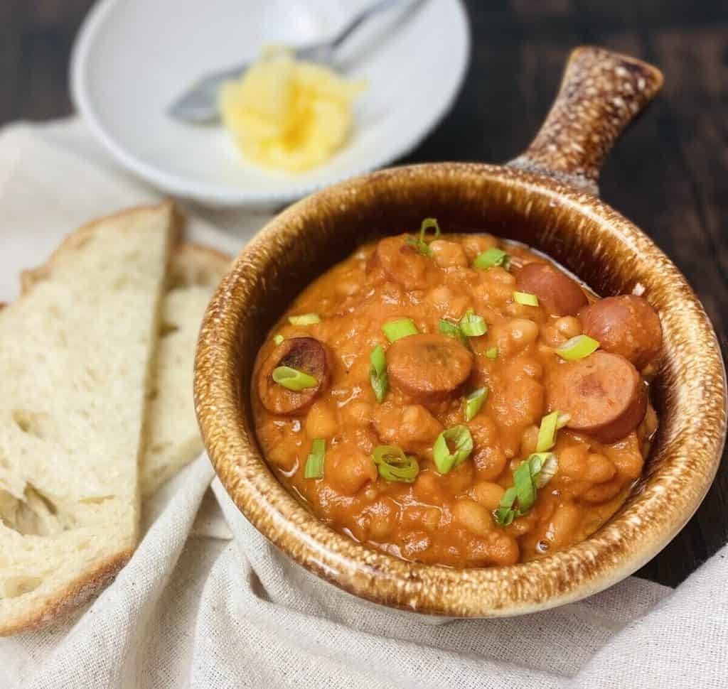 A brown bowl of soup with butter and bread in the background.