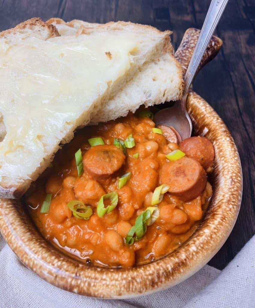 Bowl of tomato soup with franks and beans with buttered bread and a spoon.