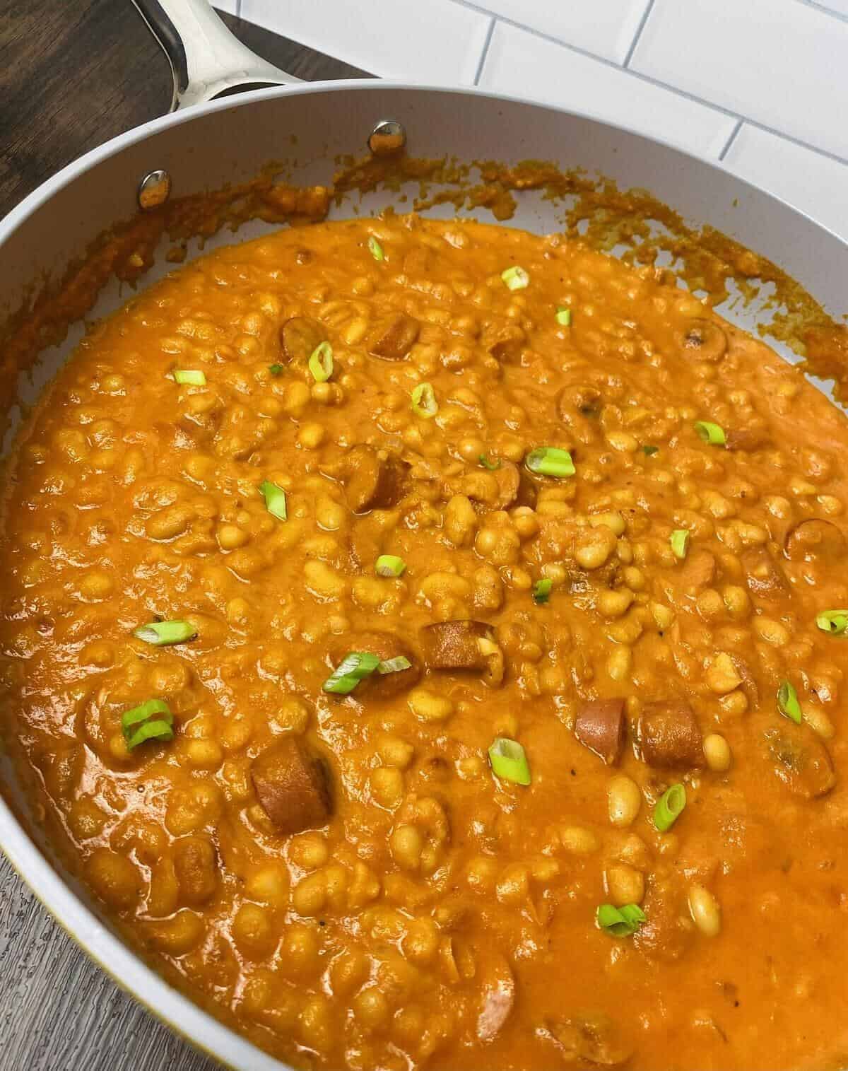 A large pan filled with creamy tomato soup with franks and beans.