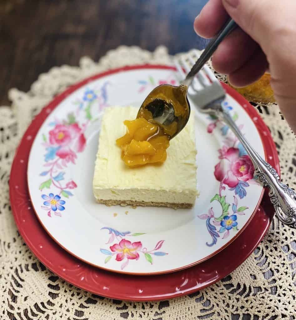 A spoon adding peach compote to a piece of peaches and cream dessert.