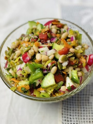 Chopped vegan salad in a clear bowl on a lace tablecloth.