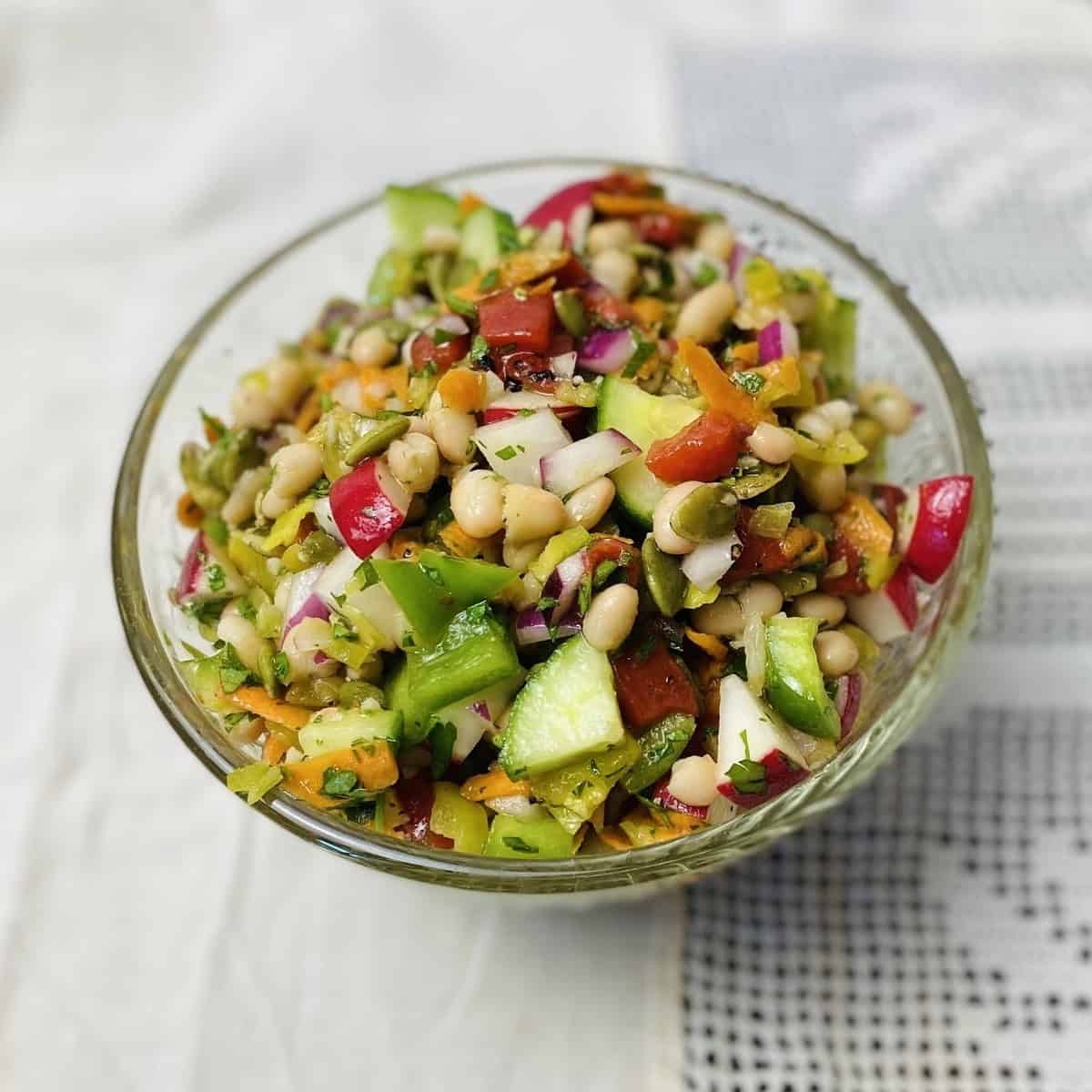 Chopped vegan salad in a clear bowl on a lace tablecloth.