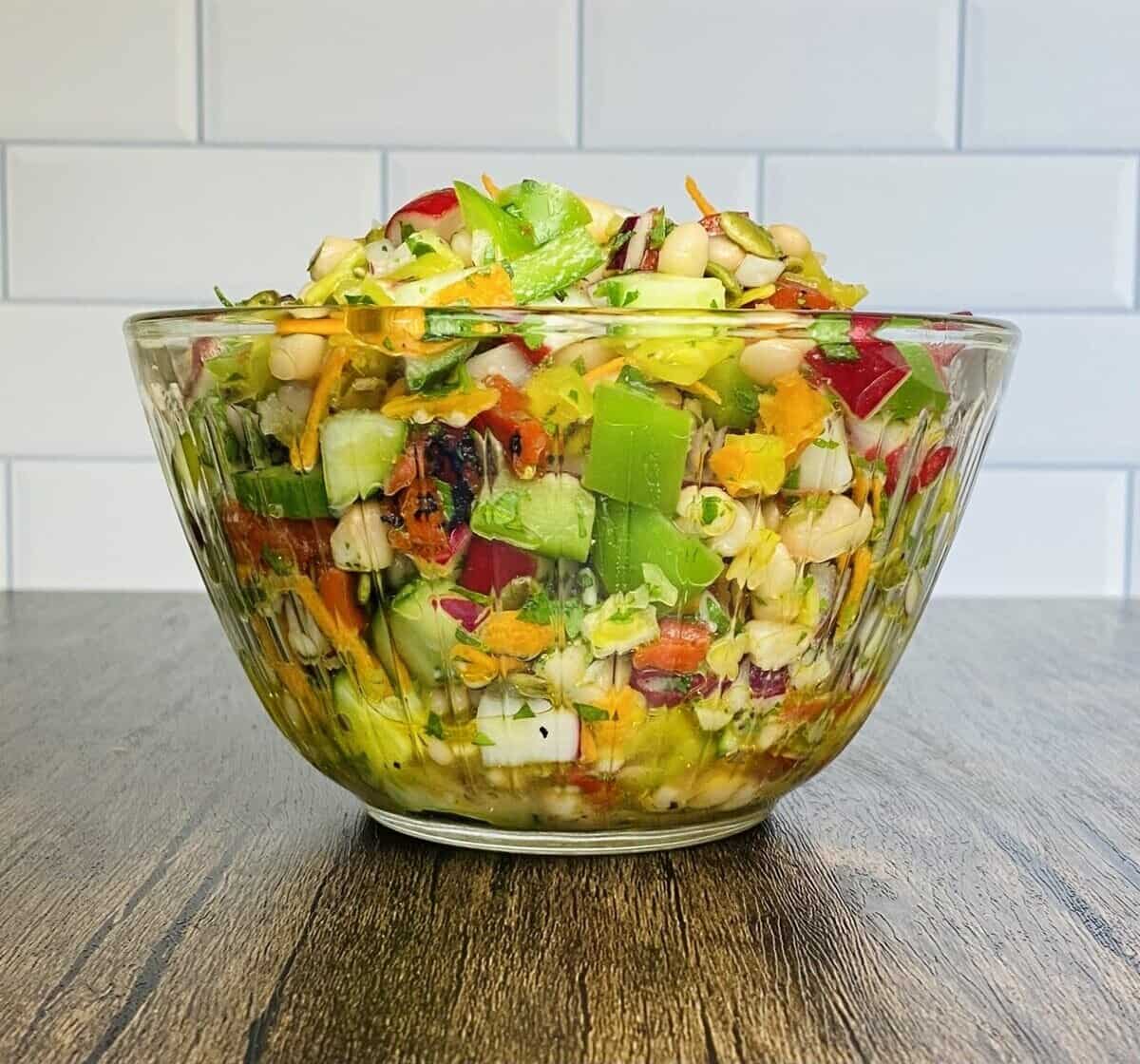 A side view of a clear bowl filled with chopped vegan salad.