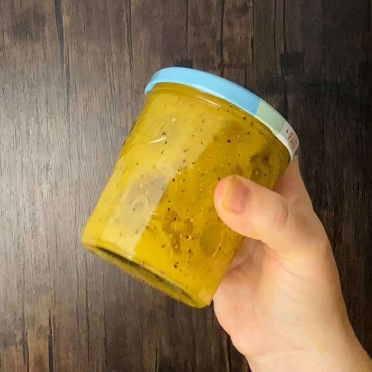 A hand holding a mason jar filled with dressing ingredients.